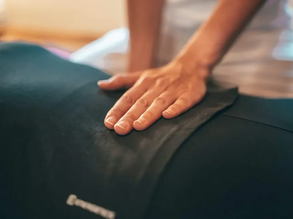 A massage therapist's flat hand pressing along a person's back as they lie on a treatment table in a warmly lit clinic room
