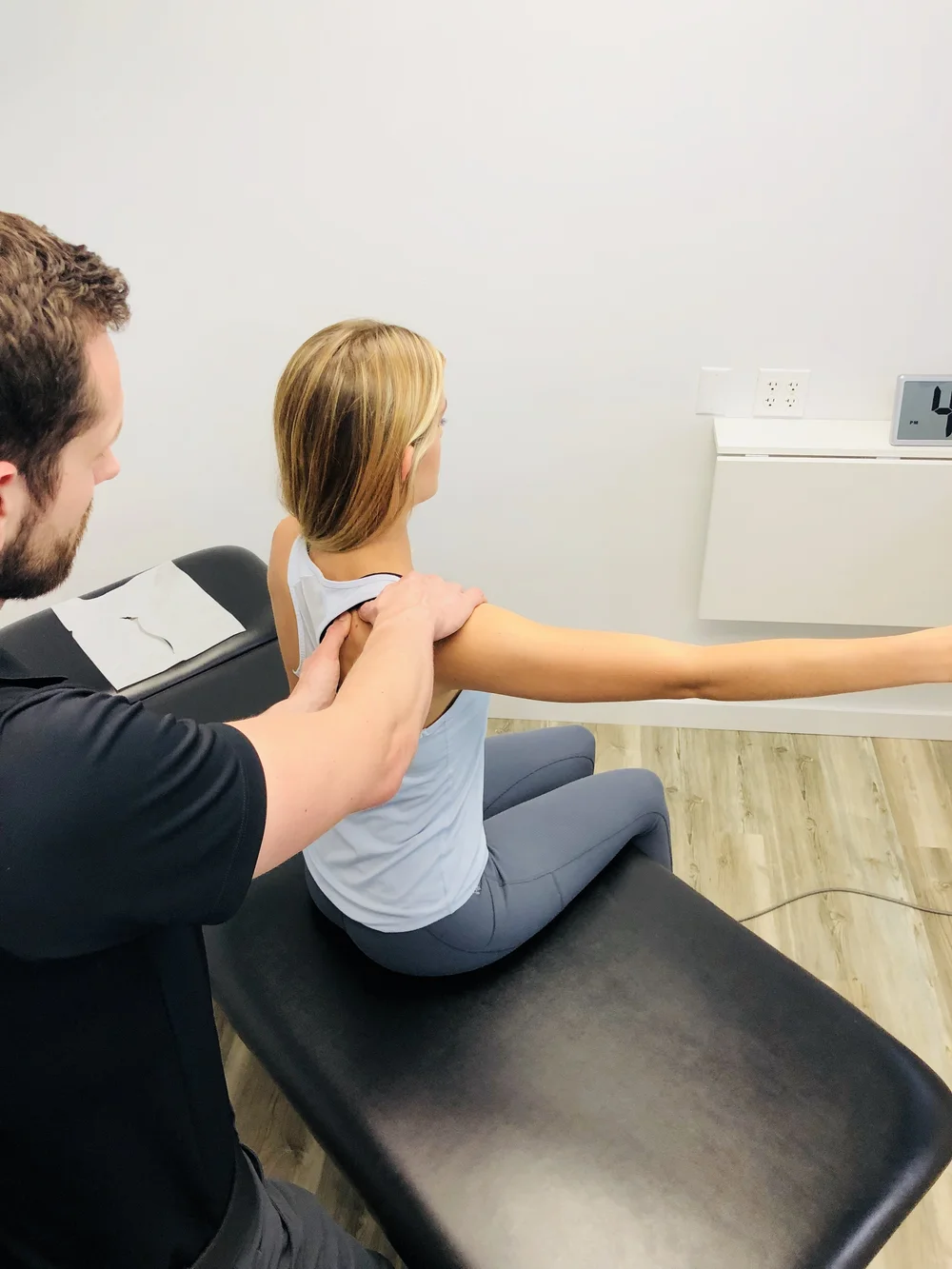 A Radius provider supports a seated patient's shoulder and guides her extended arm during an orthopedic and neuromuscular movement test